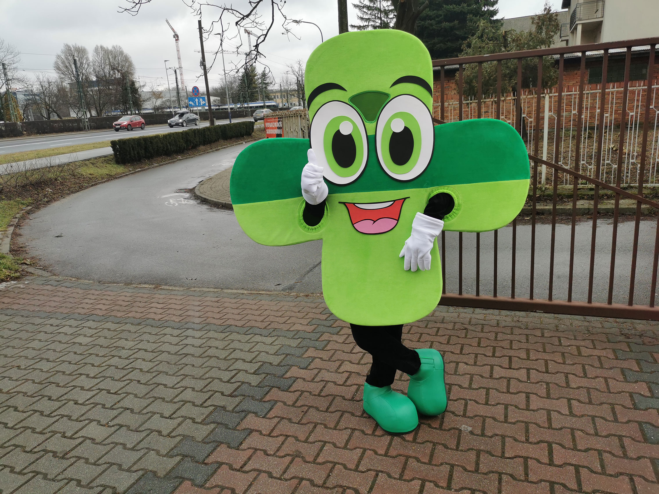 Na fotografii widnieje kostium reklamowy w postaci zielonej koniczyny pozujący do zdjęcia obok siedziby firmy Elabika